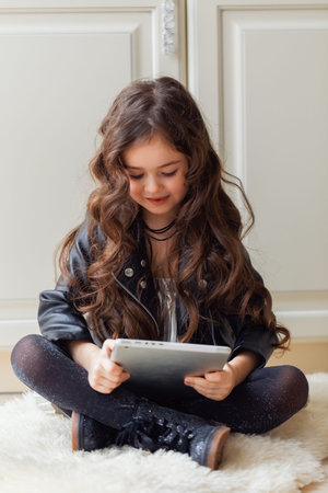 Little girl is playing game using tablet while sitting on floor in her room