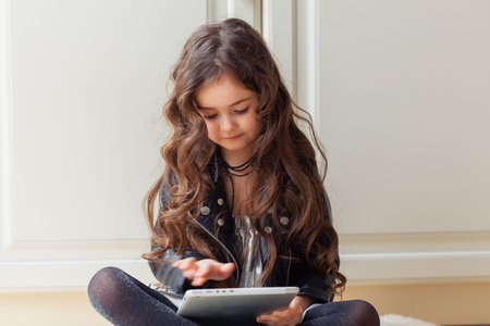 Little girl is playing game using tablet while sitting on floor in her room