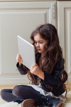 Little girl is playing game using tablet while sitting on floor in her room