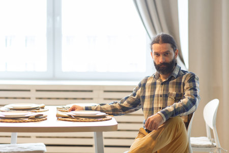 Portrait of a cute long-haired man with a beard weared in checkered shirt and light brown trousers...