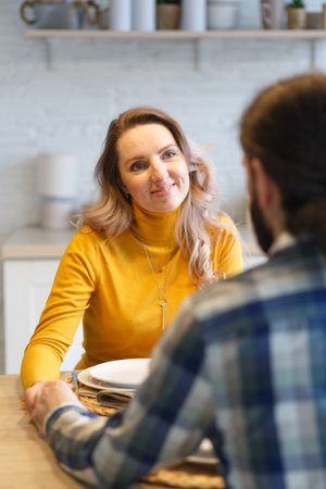 Beautiful couple having a conversation while looking at each other sitting at the table in a kitchenの写真素材