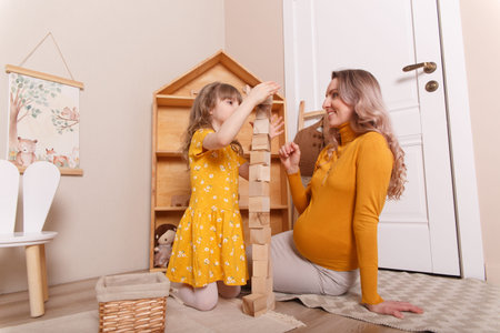 A pregnant woman plays in the nursery with her daughter. They build a tower out of wooden blocks.の写真素材