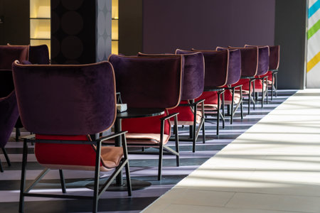 A row of tables with soft comfortable violet chairs for visitors to the food court of a modern...