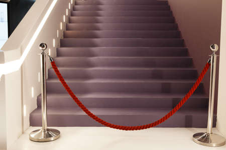 Silver racks with red restraining rope. Barrier, enclosed VIP area, protected enterance, private event, luxury gala concept. Stairs to the penthouse.の写真素材