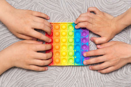 Two kids push sensory popit at the same time on gray background. Rainbow silicone sensory fidget. New popular trendy silicone toy.の写真素材