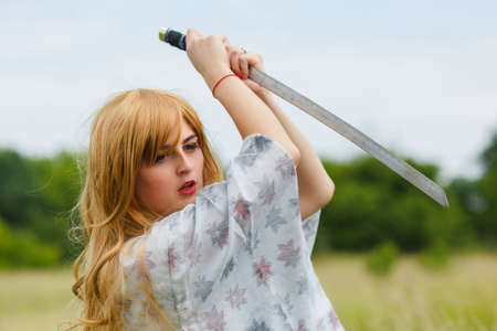 Young asian woman in traditional kimono trains fighting techniques with katana sword outdoors, samurai warrior girlの写真素材