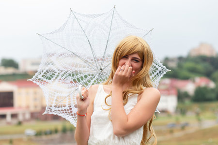 A girl in a white dress with white sun umbrella posing on city background.の写真素材