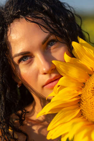 Close-up portrait of a young woman looking out from behind a large sunflower. Summertime concept.の写真素材