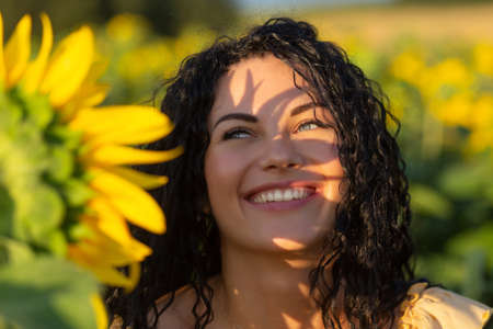 Close-up portrait of a young woman looking out from behind a large sunflower. Summertime concept.の写真素材