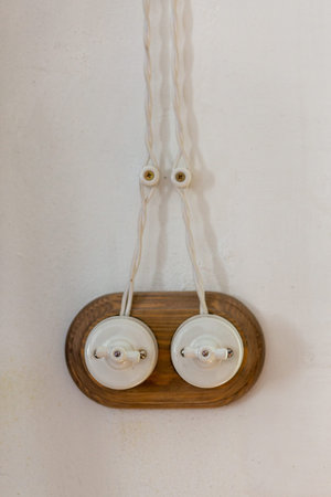 A old-fashioned switch wires is installed on a empty plastered white wall. Electric switch with two...