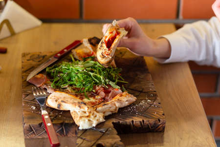 Close-up of the hands of a girl who eats bruschetta or pizza with herbs and sauce in a cafeの写真素材