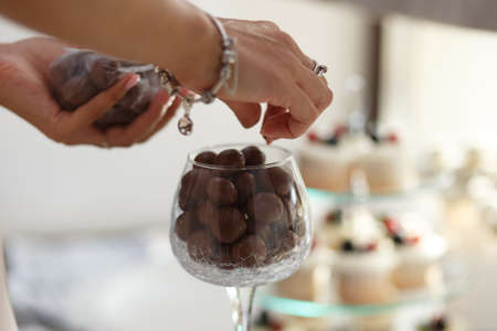 Female hands serving plate with round chocolate candies in wine glass on festive tableの写真素材