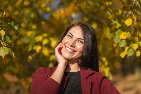 Portrait of a joyful young woman enjoying in the autumn park. Beautiful brunette girl in autumn red coat and black sweater. Relax in nature. High quality photoの写真素材