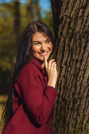 Portrait of a joyful young woman enjoying in the autumn park. Beautiful brunette girl in autumn red coat and black sweater. Relax in nature. High quality photoの写真素材