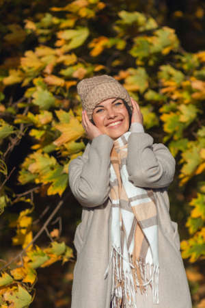 Portrait of a joyful young woman enjoying in the autumn park. Beautiful brunette girl in autumn grey coat and knitted hat. Relax in nature. High quality photoの写真素材