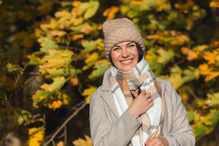 Portrait of a joyful young woman enjoying in the autumn park. Beautiful brunette girl in autumn grey coat and knitted hat. Relax in nature. High quality photoの写真素材