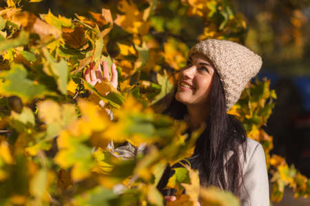 Portrait of a joyful young woman enjoying in the autumn park. Beautiful brunette girl in autumn grey coat and knitted hat. Relax in nature. High quality photoの写真素材