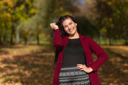 Portrait of a joyful young woman enjoying in the autumn park. Beautiful brunette girl in autumn red coat and black sweater. Relax in nature. High quality photoの写真素材