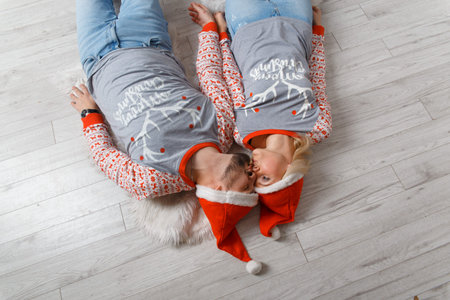 Beautiful happy couple in Christmas scenery. Weared in funny sweaters and hats. Laying down on the...