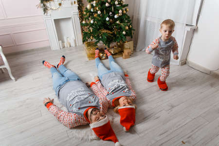 Happy family near christmas tree having fun on the floor. Christmas celebration at home. Mom, Dad and son weared in casual. Happy family funny playing on a bed. Christmas decorated grey interiorの写真素材