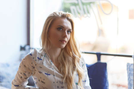 Young pretty woman wearing in white blouse and jeans resting on windowsill in cafeの写真素材
