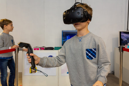 Eight years boy wearing VR headset, holding controllers in hands and enjoying new experience in...