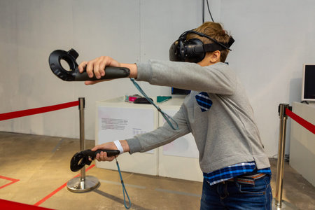 Eight years boy wearing VR headset, holding controllers in hands and enjoying new experience in...