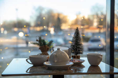 A table in a cafe with a view of the evening city. The table is set for a Christmas tea party. Garlands are burning on the windowの写真素材