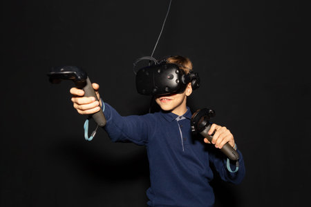 Eight years boy wearing VR headset, holding controllers in hands and enjoying new experience in...