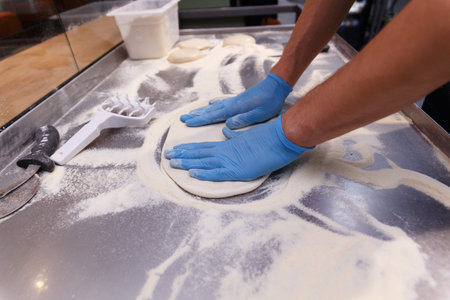 Making dough by male hands in blue rubber gloves on table background. Pizza maker prepares a pizza...