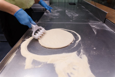 The cook processes the pizza dough with a special roller with spikes to make the dough fluffy and crispy.の写真素材