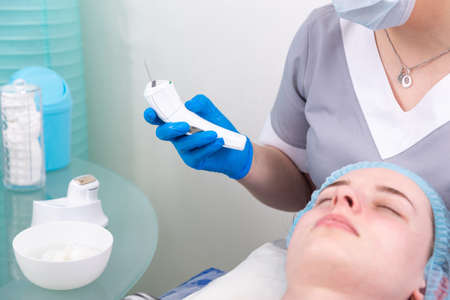 Ultrasound facial peeling. Young woman getting ultrasonic peel skin with skin scrubber at cosmetology clinic.の写真素材