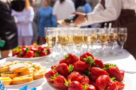 A banquet table with wine glasses and plates with snacks. Waiter fill glasses with champagne. Party concept. Selective focus.の写真素材