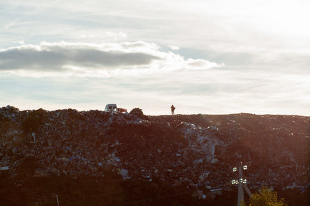 View of the city dump in the evening. A worker stands on a mountain of garbage.の写真素材