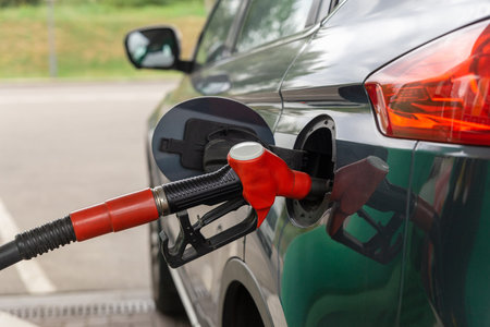Fuel nozzle to refill fuel in car at gas station. Red fuel dispenser on gray car in petro station.