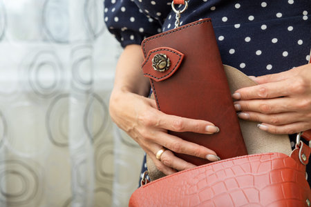 Woman takes a brown natural leather wallet out of her purse. Wallet made of genuine leather, a...
