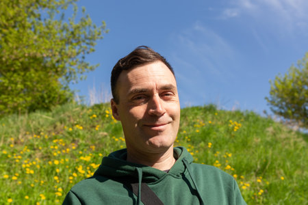 Portrait of a young attractive man in the nature. Young serious man posing on green hill with dandelions in sunlight.の写真素材
