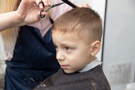 Nice european little boy getting hairstyle in barbershop. Hairdresser makes a hairstyle for a boy.の写真素材