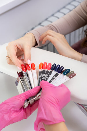 Professional manicurist showing colorful nail polish to check the finish result. Nail technician presenting color palette of nail samples in beauty salon store. Beauty and fashion concept.の写真素材