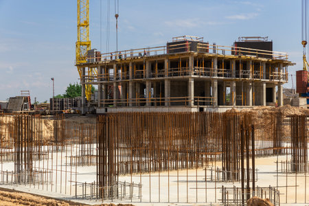 Crane and building construction site against blue sky. Concrete building under construction. In the foreground is the steel reinforcement of the foundation of the future building.の写真素材