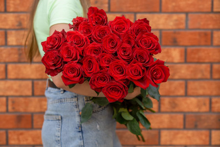 Woman holding luxury bouquet of fresh red roses against the background of brick wall. Mono bouquet of red roses in womans hands.の写真素材
