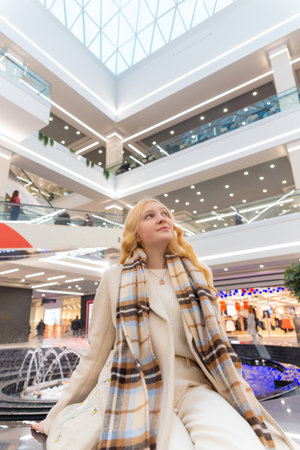 Girl sitting on the parapet at the mall near the fountain. Young woman restinag and waiting for her friends.の写真素材