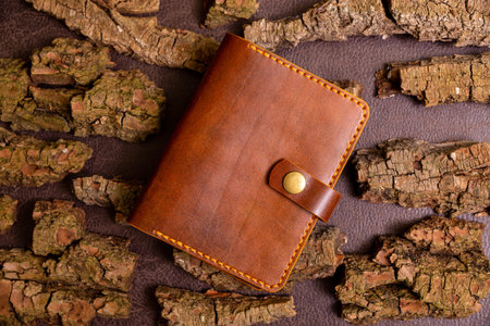 Closed brown mens wallet for cash and credit cards on leather background with pine bark.