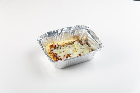 Pasta, conchiglie pasta, with a tomato and basil sauce topped with cheese in a foil takeaway tray. Healthy restaurant lunch. Daily take away meals. Baked tomatoes with low fat cheese and greens in foil box. Isolated on white background, cutoutの写真素材