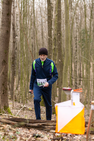 Grodno, Belarus - 26 March, 2023: Strong elderly caucasian man wearing sportswear running through a forest during exercise in outdoor orienteering Grodno Forest Day. Belarus, hobby sport.のeditorial素材