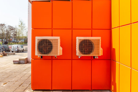 Two air compressors installation on orange wall outside. Air condenser outdoor unit for heat removal. Cooling equipment with two fans on the outside wall of modern building.の写真素材