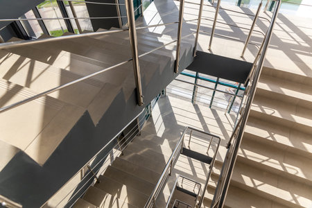 Stairs in a concrete office building in neutral tones, covered with ceramic tiles, with shiny metal...