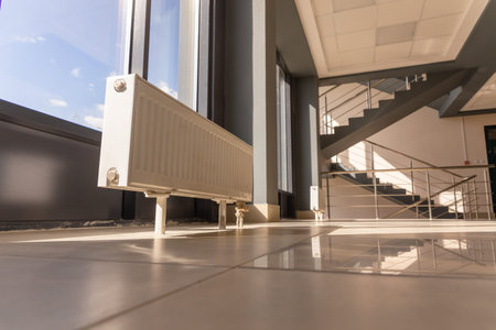 Vertically installed central heating radiator on the floor at the fully glazed exterior wall of the...