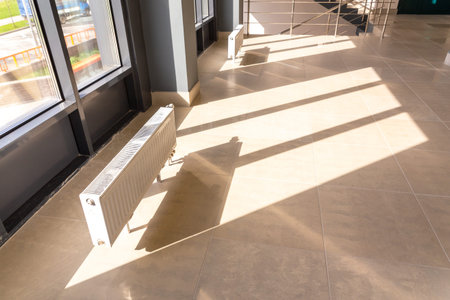 Vertically installed central heating radiator on the floor at the fully glazed exterior wall of the...