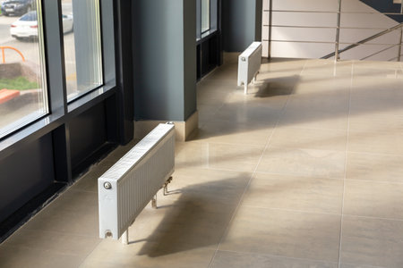 Vertically installed central heating radiator on the floor at the fully glazed exterior wall of the office building. A white radiator in a room with a window and a blue sky behind it.の写真素材